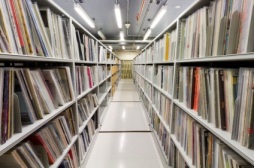 Colour photograph of stacks. There is an aisle down the middle with rows of books on either side. 