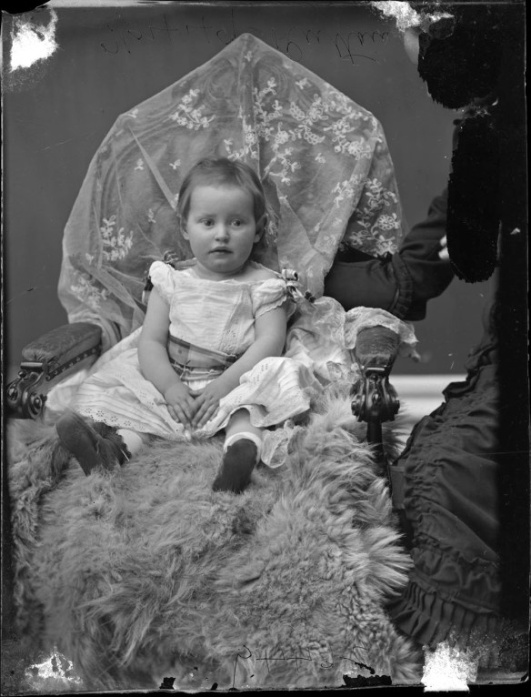 Black-and-white photograph of a young child with the mother to the right, partially blacked out.