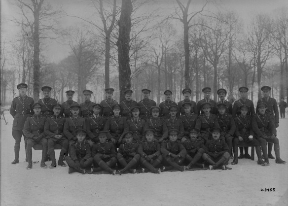 A black-and-white photograph of a group of soldiers standing and sitting in front of trees in the winter.