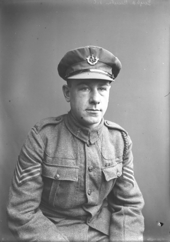 A black-and-white photograph of a seated soldier in uniform and cap. 