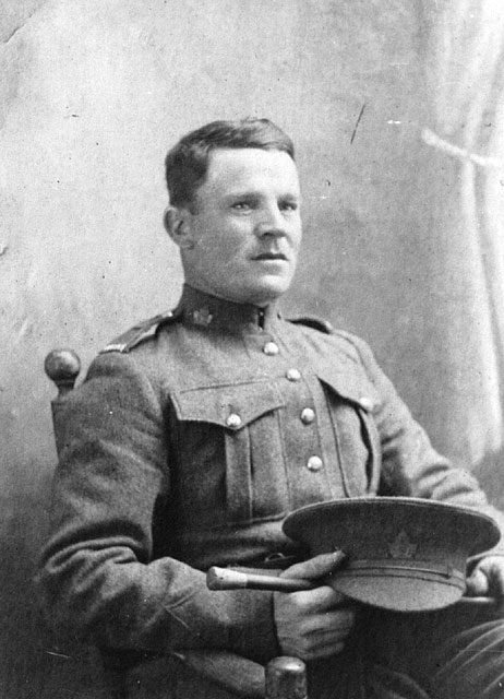 A black-and-white portrait photograph of a seated soldier who holds his cap and swagger stick on his lap.