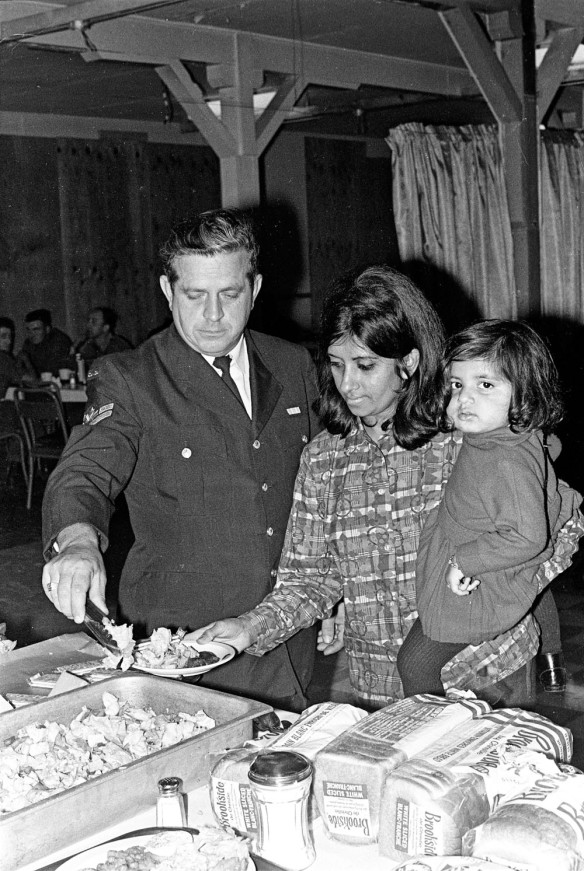A black-and-white photograph of a man in a uniform serving food to a woman holding a small child.