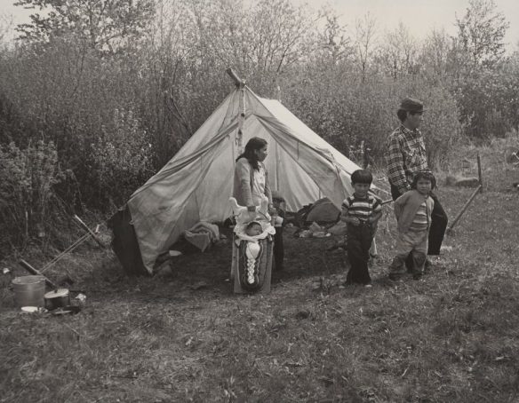 First Nation family with a baby secured onto a cradleboard in front of a tent near Lac Seul in Ontario.