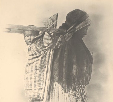 First Nation woman with a baby on a cradleboard on her back.