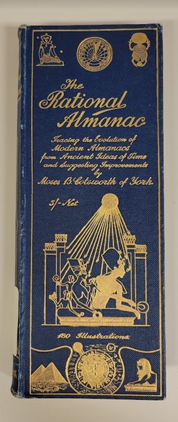 A blue hardcover book. The title, printed in gold lettering, is “The Rational Almanac Tracing the Evolution of Modern Almanacs from Ancient Ideas of Time and Suggesting Improvements by Moses B. Cotsworth of York. Five shillings net. 180 Illustrations.” The cover is decorated with Egyptian elements, including pyramids, a sphinx, sundials and a portrait of a pharaoh under a sun, all in gold.