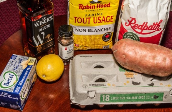 Photo featuring ingredients for sweet potato pie: butter, whisky, flour, sugar, lemon, nutmeg, eggs, and sweet potato.