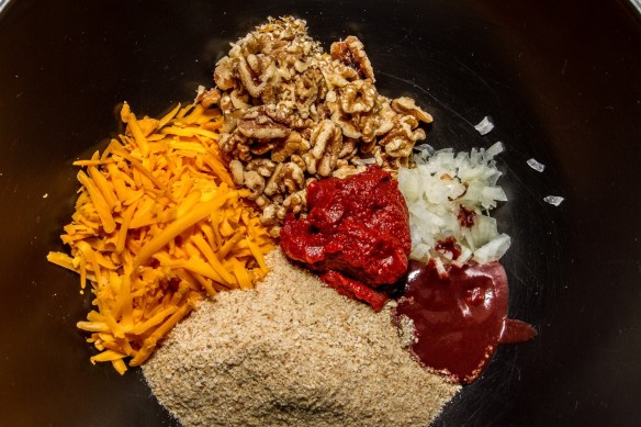 All ingredients placed separately in a bowl: cheddar cheese, walnuts, tomato paste, onions, hot sauce and breadcrumbs.